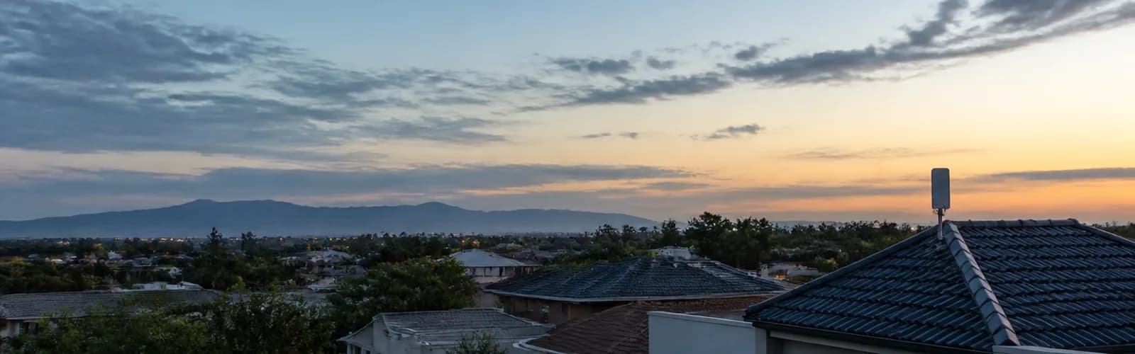Suburban rooftops at dusk with a small wireless antenna on one roof