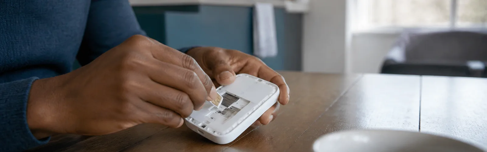 Hands inserting a SIM card into a portable MiFi router on a kitchen table
