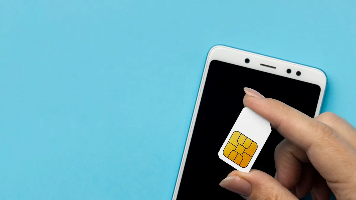 A hand holding a SIM card next to a smartphone